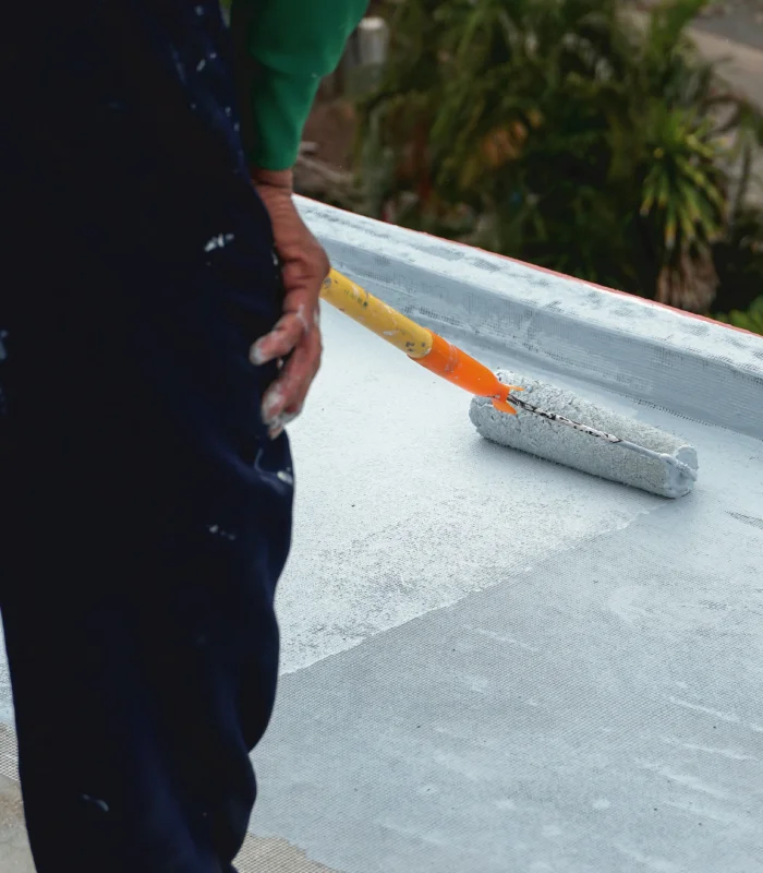 A man skillfully applies paint to a roof using a paint roller, showcasing his meticulous effort and dedication to home improvement.