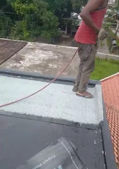 A man is using a hose while working on a roof, demonstrating skill and focus in his task.